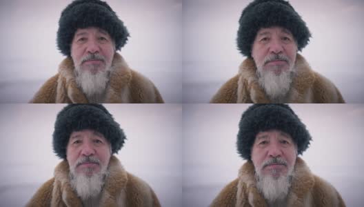 冬日里，一个留着胡子的土著老人站在户外看着镜头。老家伙头照，戴着帽子，穿着皮草大衣，表情严肃。高清在线视频素材下载