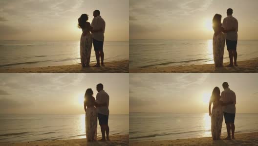 一对年轻的夫妇站在海滩上，欣赏海面上的日落高清在线视频素材下载