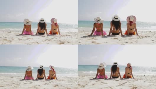 后视图三个女孩在海滩上穿着比基尼和草帽享受日光浴，女性游客在暑假高清在线视频素材下载
