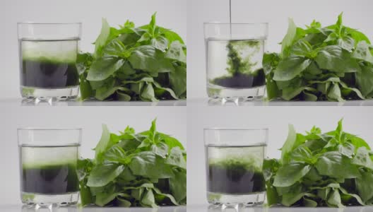 叶绿素提取物和罗勒倒在纯净的水在玻璃的白色背景和绿色有机罗勒草本。种植新鲜植物健康食物超级食物概念，排毒饮食，慢动作高清在线视频素材下载