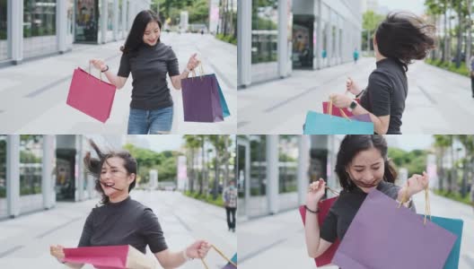 微笑年轻的亚洲女人与购物彩袋在商场背景。用智能手机在网上购物，站在商场大楼里微笑。生活方式的概念。慢镜头4 k。高清在线视频素材下载