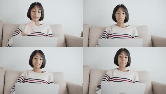 手持。快乐的亚洲小女孩在笔记本电脑上视频通话，并在上午坐在家里客厅的沙发上与导师招手打招呼高清在线视频素材下载