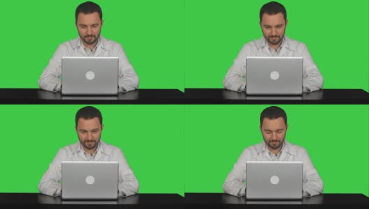 微笑的男医生坐在桌子上，笔记本电脑在绿色屏幕上，Chroma Key高清在线视频素材下载
