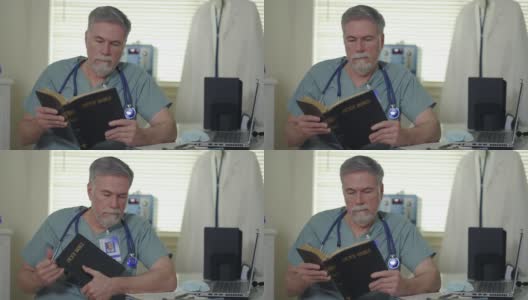 在一个小诊所里，一位基督教医生坐在他的办公桌前阅读《圣经》，以寻求鼓励和安慰。高清在线视频素材下载