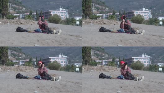 在阳光明媚的春天，带着太阳镜的女主人抱着小腊肠狗，在山上度假酒店附近的沙滩上消磨时光高清在线视频素材下载