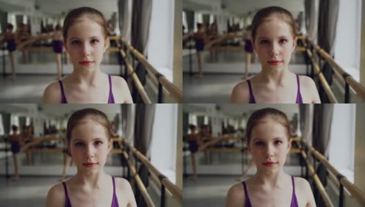 在宽敞的灯光舞厅里，化妆的年轻女孩在上芭蕾课时看着镜头微笑。艺术和童年的概念。高清在线视频素材下载