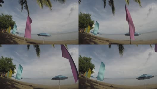 空旷的沙滩上挂着五颜六色的旗帜和遮阳伞。跟踪拍摄高清在线视频素材下载