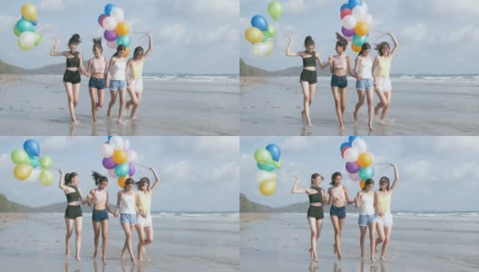 一群朋友拿着彩色气球沿着海滩散步。高清在线视频素材下载