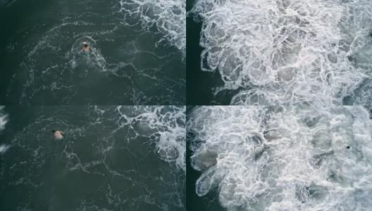 一个年轻人在暴风雨的海洋中游泳，被巨大的危险波浪击中。无人机视频正上方。高清在线视频素材下载