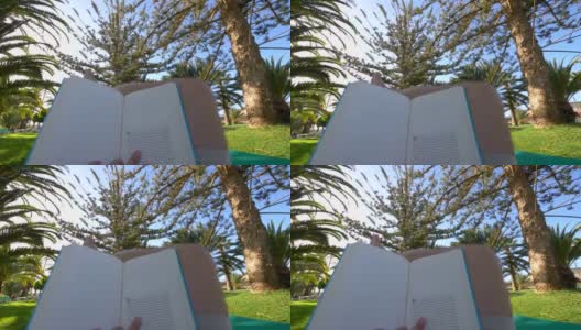 一名男子正在热带花园的日光浴床上看4K慢镜头的书高清在线视频素材下载