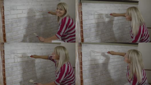 正在用油漆滚筒刷砖墙的妇女。家里装修的想法。高清在线视频素材下载