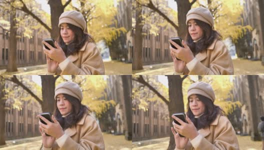 在日本用秋叶背景的智能手机旅行的亚洲女性高清在线视频素材下载