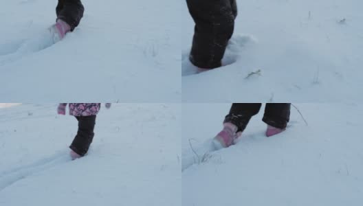 冬天，假期，游戏，家庭概念-慢动作接近婴儿走过深雪。孩子们的脚踩在雪道上。学前班的小孩穿着黑色的连体衣在寒冷的季节下雪高清在线视频素材下载