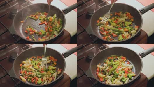 白种人的手搅拌蔬菜在煎锅与不锈钢叉子，而油炸，特写高清在线视频素材下载