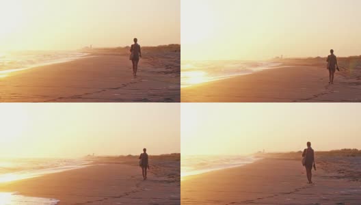 一个女人拿着一个包和沙滩鞋走在海滩在惊人的日落在夏季慢镜头。1920 x1080高清在线视频素材下载