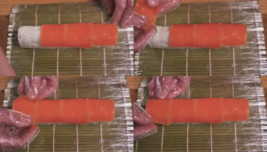 一位专业厨师将切成薄片的三文鱼放到餐桌上的寿司卷上。在一家日本餐厅，男厨师正在准备一个三文鱼寿司卷。高清在线视频素材下载