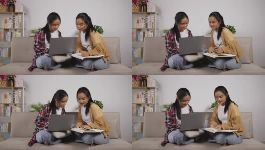 双胞胎女孩坐在沙发上看书，看笔记本电脑高清在线视频素材下载