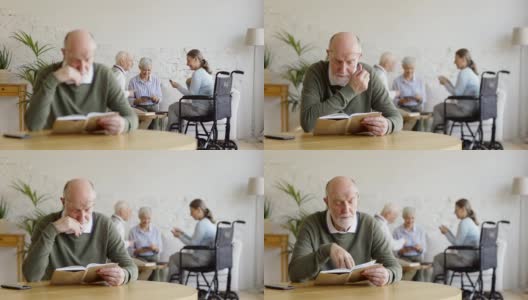 机架上聚焦了三位老人，其中两位妇女包括一位残疾人和一位男子，在敬老院享受着打牌的乐趣。聪明的老人坐在桌子旁看书高清在线视频素材下载
