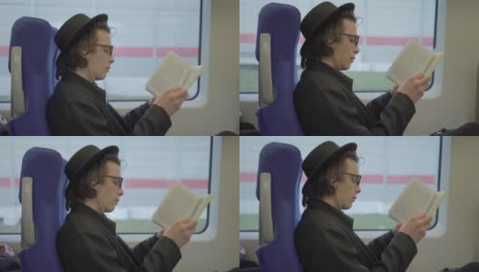 年轻帅气的男子戴着黑帽子和眼镜坐在公共交通工具上看书，千禧潮的学生喜欢在地铁里看书高清在线视频素材下载