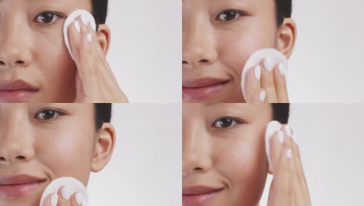 半脸肖像年轻的亚洲女士清洁脸与棉垫，白色工作室背景与空白空间高清在线视频素材下载