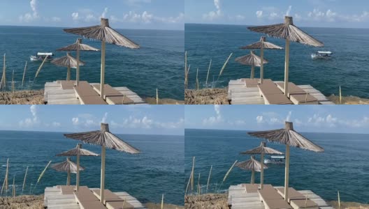 夏季地中海岩石海岸风景优美的海滩。稻草伞和舒适的阳光躺椅。船在海上航行。田园诗般的夏天海景。高清在线视频素材下载