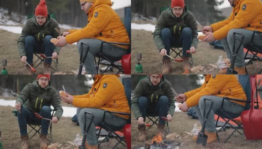 两个男人围坐在森林里的营火旁烤香肠高清在线视频素材下载