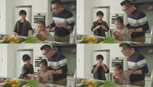 亚洲华人父女在厨房柜台边切橘子边和儿子一起吃饭高清在线视频素材下载