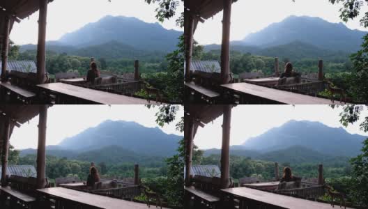 一位女游客坐在木制阳台上，看着美丽的山景高清在线视频素材下载
