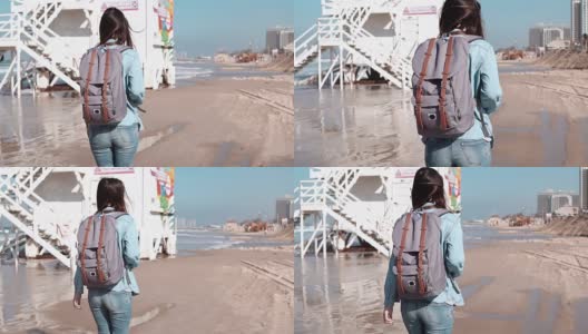 背着背包的女人走在海岸警卫哨所附近。风吹着头发。女孩在海滩上散步。慢动作高清在线视频素材下载