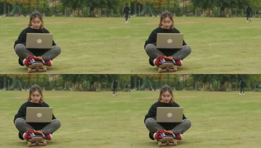 一个亚洲女大学生在校园里的草坪上用笔记本电脑高清在线视频素材下载