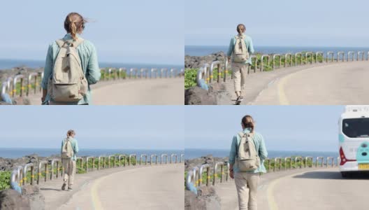 一个年轻的女游客背着背包走在有海景的路上。高清在线视频素材下载