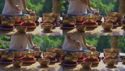 一名亚洲神药女大师表演藏式碗疗愈仪式的超慢镜头。用西藏唱碗冥想。她坐在凉亭里冥想，背景是美丽的瀑布高清在线视频素材下载