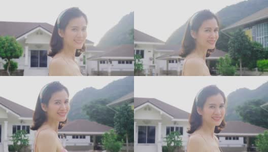 肖像亚洲美丽的年轻女子站在户外的房子前面，微笑的脸，笑。放松女孩感到高兴，高兴和有快乐的时刻在假期在傍晚日落时间。高清在线视频素材下载