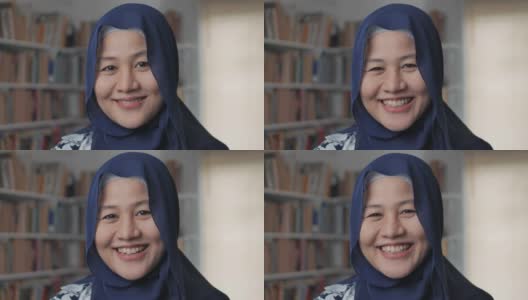 快乐的亚洲穆斯林妇女戴着头巾对着镜头微笑，女学生在图书馆高清在线视频素材下载