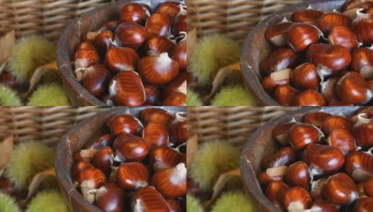 这是一个木碗里新鲜采摘的栗子的特写，背景是模糊的绿色刺猬。十月，栗子收获的季节。典型的秋季新鲜水果。高清在线视频素材下载