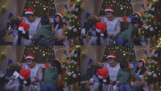 快乐的一家人带着女儿戴着圣诞帽，在圣诞节的时候聚在一起，享受打开礼品盒的乐趣高清在线视频素材下载
