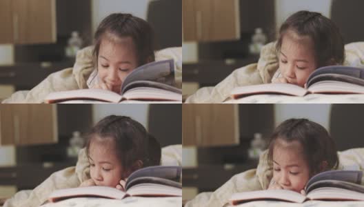 近距离4K的可爱的5岁亚洲女孩，她正在床上看书，美丽的黄色灯光从一盏灯。就寝时间是孩子学习、放松和发展创造力的时间。高清在线视频素材下载