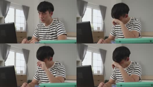 被隔离在卧室的亚洲男学生在家里用笔记本电脑观看视频讲座时，眼睛受到了刺激，正在揉眼睛高清在线视频素材下载