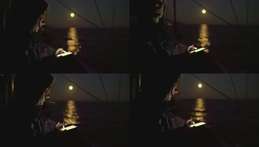 一名女子在满月背景下的帆船上使用4K智能手机高清在线视频素材下载