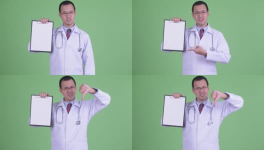 亚洲男人医生的工作室肖像看起来悲伤和拇指向下，而持剪贴板与复制空间在绿色背景高清在线视频素材下载