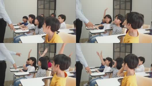 亚洲老师在学校的教室里教孩子们。小男孩和小女孩一起举手接受评论。教育理念、经验学习和技能发展。高清在线视频素材下载
