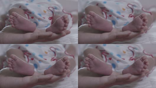 当她的宝宝在温柔和爱中睡觉时，妈妈靠近新生儿的脚。幸福的家庭的概念。高清在线视频素材下载