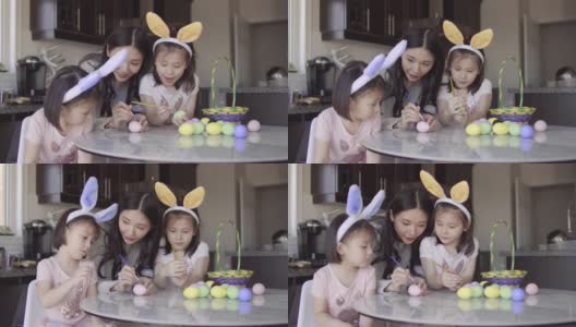妈妈帮助两个亚裔女孩给复活节彩蛋着色高清在线视频素材下载