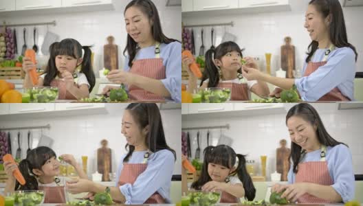 4k，年轻的亚洲母亲和女儿快乐和乐趣准备蔬菜和水果沙拉在一个现代化的白色厨房。女儿做饭时心情愉快。高清在线视频素材下载