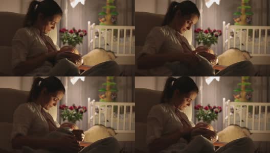 年轻美丽的母亲，在昏暗的灯光下给她的新生儿喂奶。妈妈母乳喂养婴儿。高清在线视频素材下载
