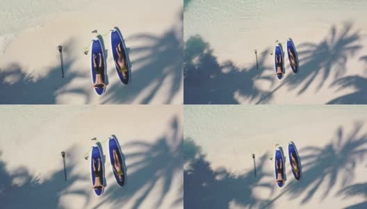 一对年轻夫妇躺在桨板上，在棕榈树的树荫下高清在线视频素材下载