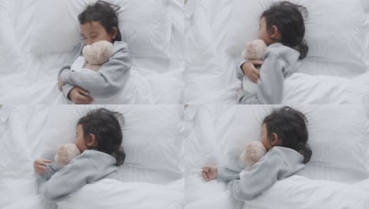 一个亚洲小女孩在卧室里睡觉，抱着泰迪熊高清在线视频素材下载
