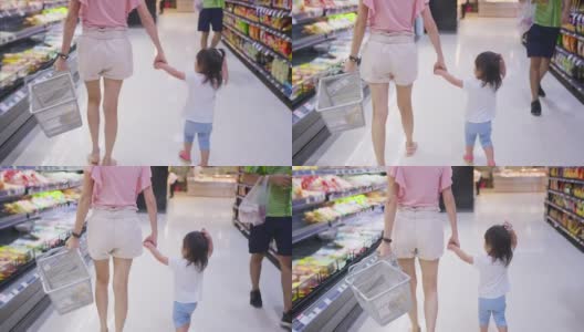 年轻的亚洲美丽的母亲拿着购物篮和她的孩子走在超市。她正在为她的小孩挑选架子上的食物。健康购物在零售商店。高清在线视频素材下载