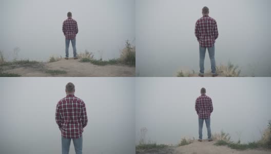 年轻的白人男子的背影，他站在河边的悬崖上，望着远方。现场镜头放大到一个享受户外自然美景的人。独处和生活方式的概念。高清在线视频素材下载