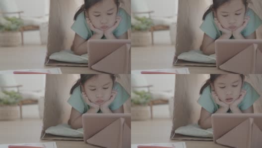 混合亚洲女孩远程学习，用数码平板电脑视频通话在一个再利用的纸板帐篷在家里，使用缩放在线虚拟课堂，家庭教育，新常态概念高清在线视频素材下载